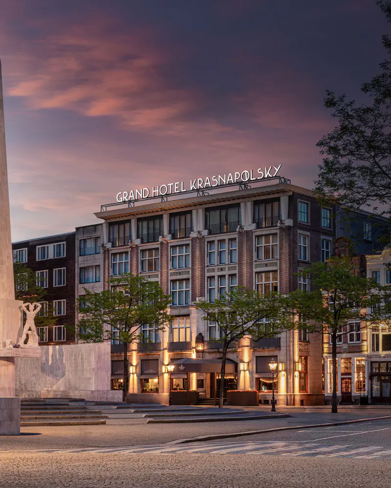 De gevel aan de Dam bij schemering, met het Nationaal Monument op de voorgrond