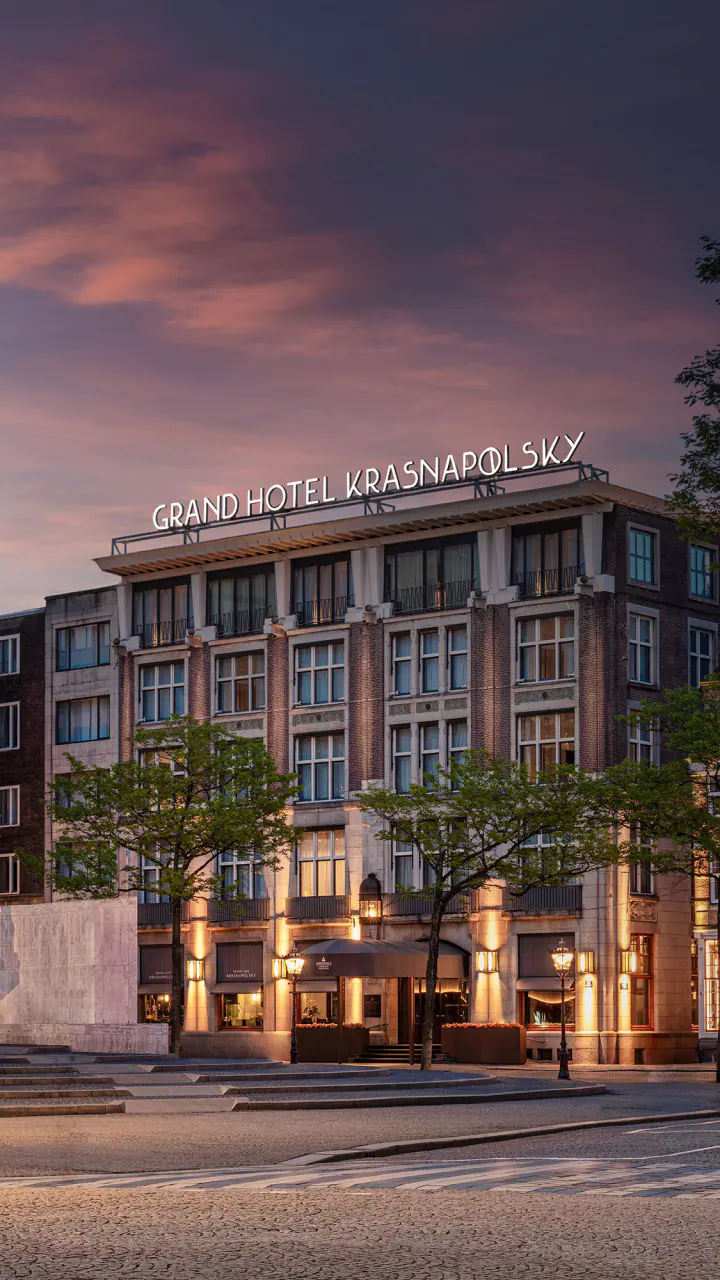 De gevel van Grand Hotel Krasnapolsky aan de Dam bij schemering, met het Nationaal Monument op de voorgrond