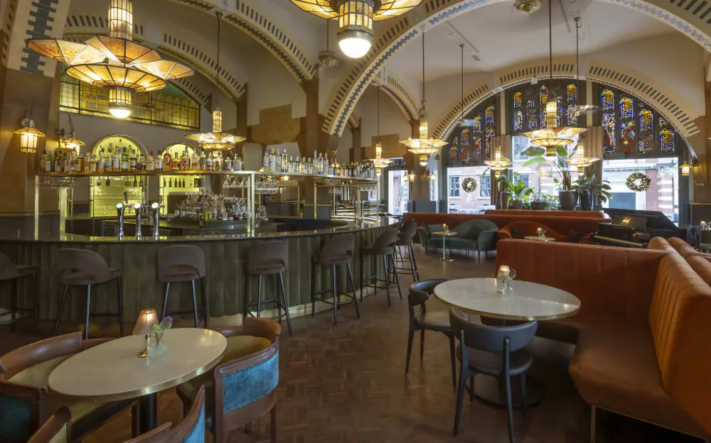 De zaal van Café Americain met tafels onder grote art-decolampen