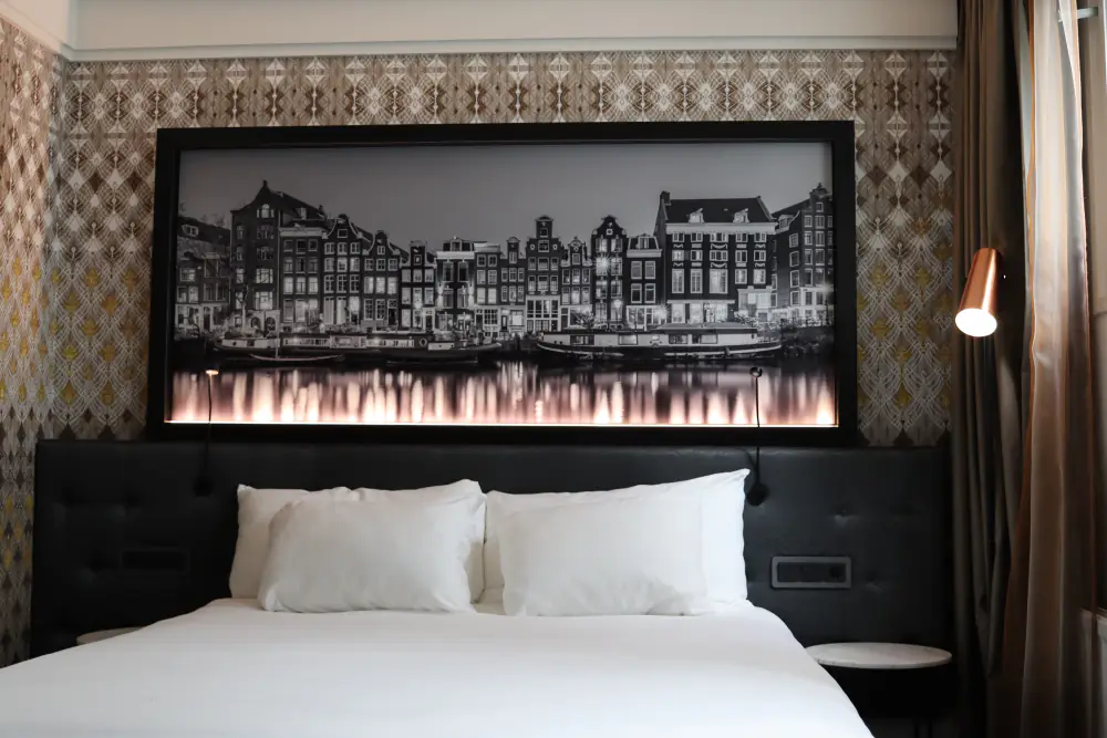 Een hotelkamer in Clayton Hotel Amsterdam American met een tweepersoonsbed en een foto van Amsterdam boven het bed