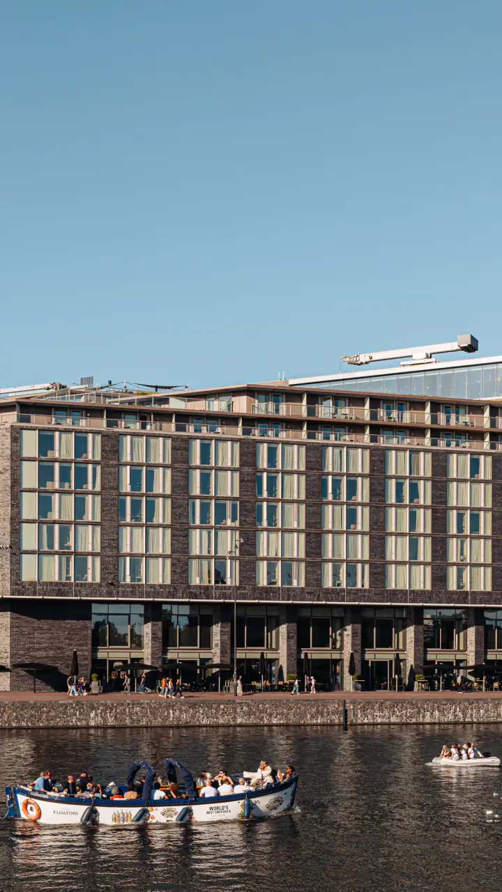 Het hotelgebouw van DoubleTree aan het Oosterdok op een zonnige dag, met een rondvaartboot op het water ervoor