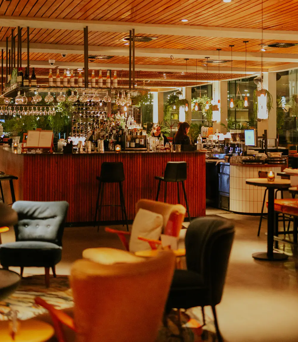 De bar van PARK met fauteuils, planten en een rode toog