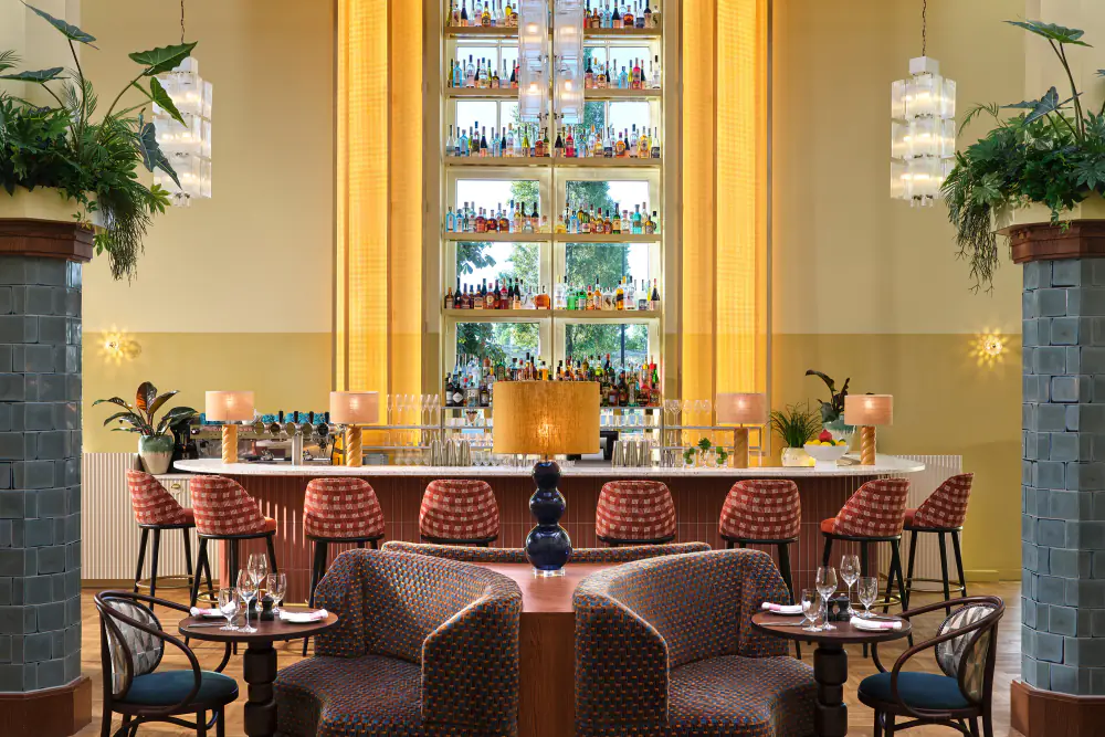 De bar van Breman Brasserie met roze krukken, lage fauteuils en een verlichte drankenkast