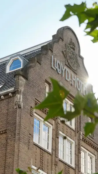 De bakstenen trapgevel van het Lloyd-gebouw met de letters Lloyd Hotel en een wapen, tussen groene bladeren in de zon