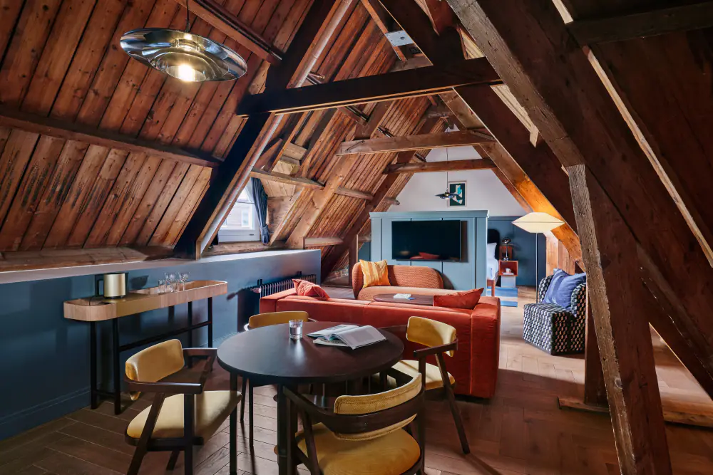 Een studio onder de houten kap van het Lloyd-gebouw, met een zithoek en een bed