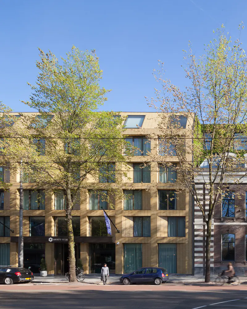 Nieuwbouw in lichte baksteen naast een historisch pand met een begroeid dak, aan de Sarphatistraat
