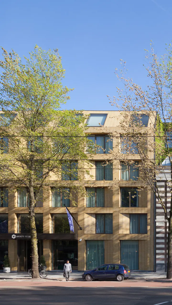 De gevels van Hyatt Regency aan de Sarphatistraat: nieuwbouw in lichte baksteen naast een historisch pand met een begroeid dak