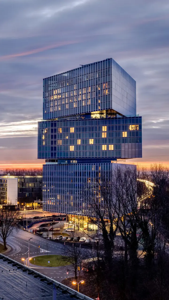 De gestapelde glazen toren van nhow Amsterdam RAI in de schemering, met verlichte ramen en de ringweg ernaast