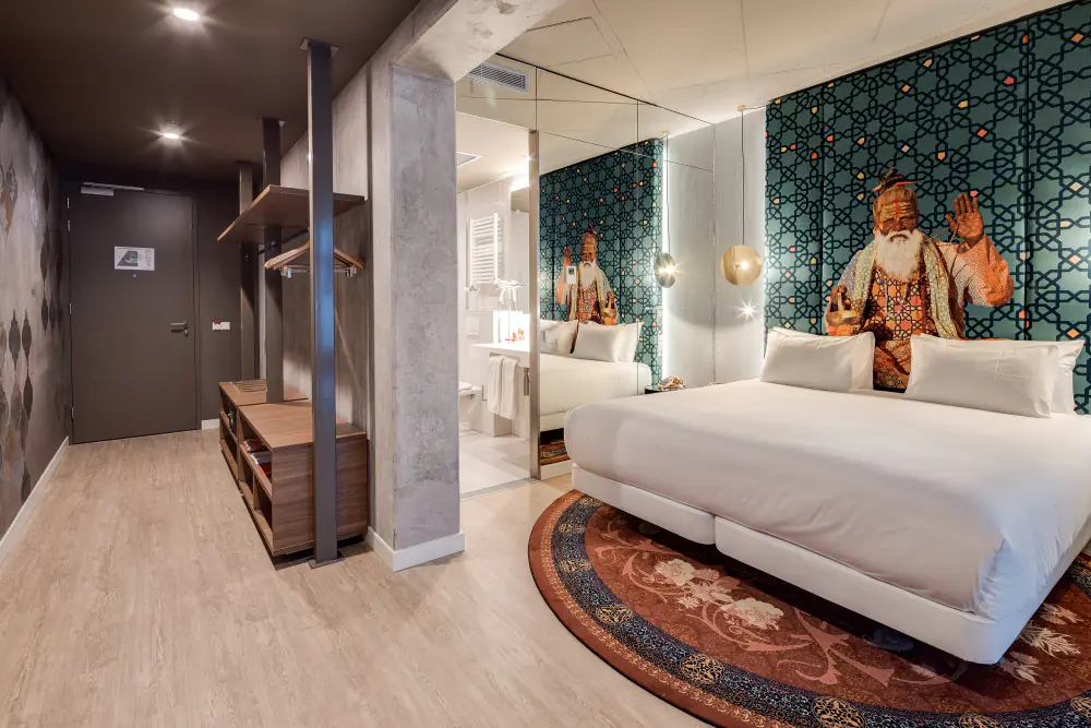 Een hotelkamer van nhow met een tweepersoonsbed en een wandschildering van figuren in kleurige kleding