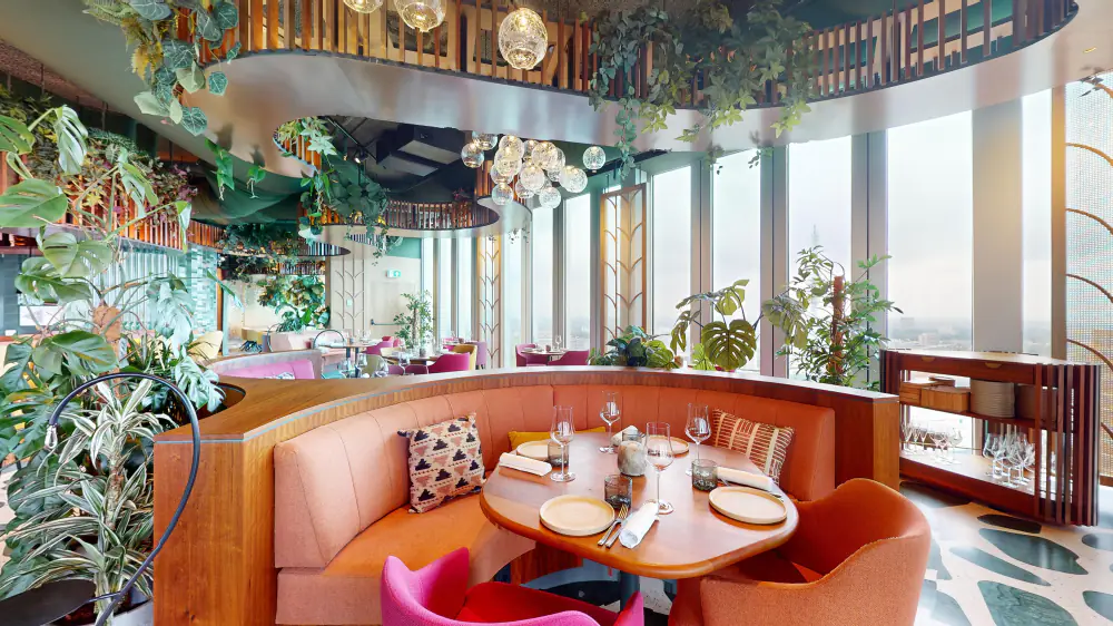 Een ronde tafel in een roze bank bij de ramen van Selva, tussen de planten