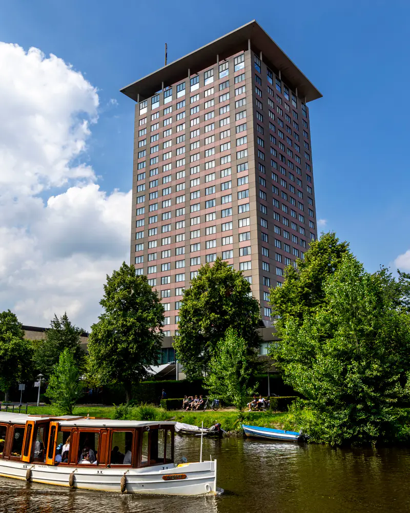 De toren boven de bomen langs het water, met een salonboot op de voorgrond