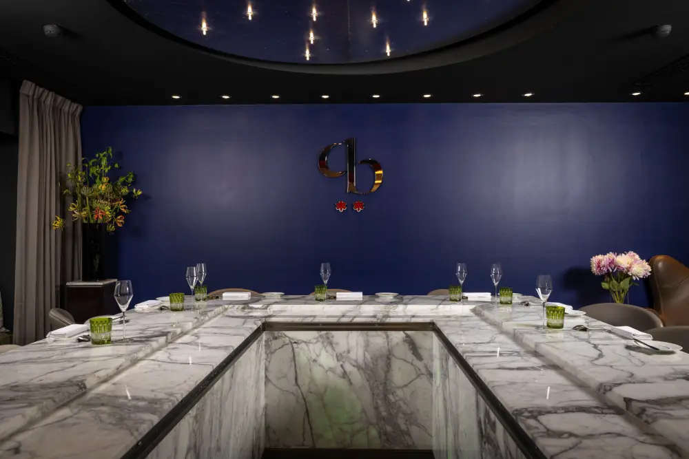 Een donkerblauwe zaal in Ciel Bleu met een lange, gedekte tafel