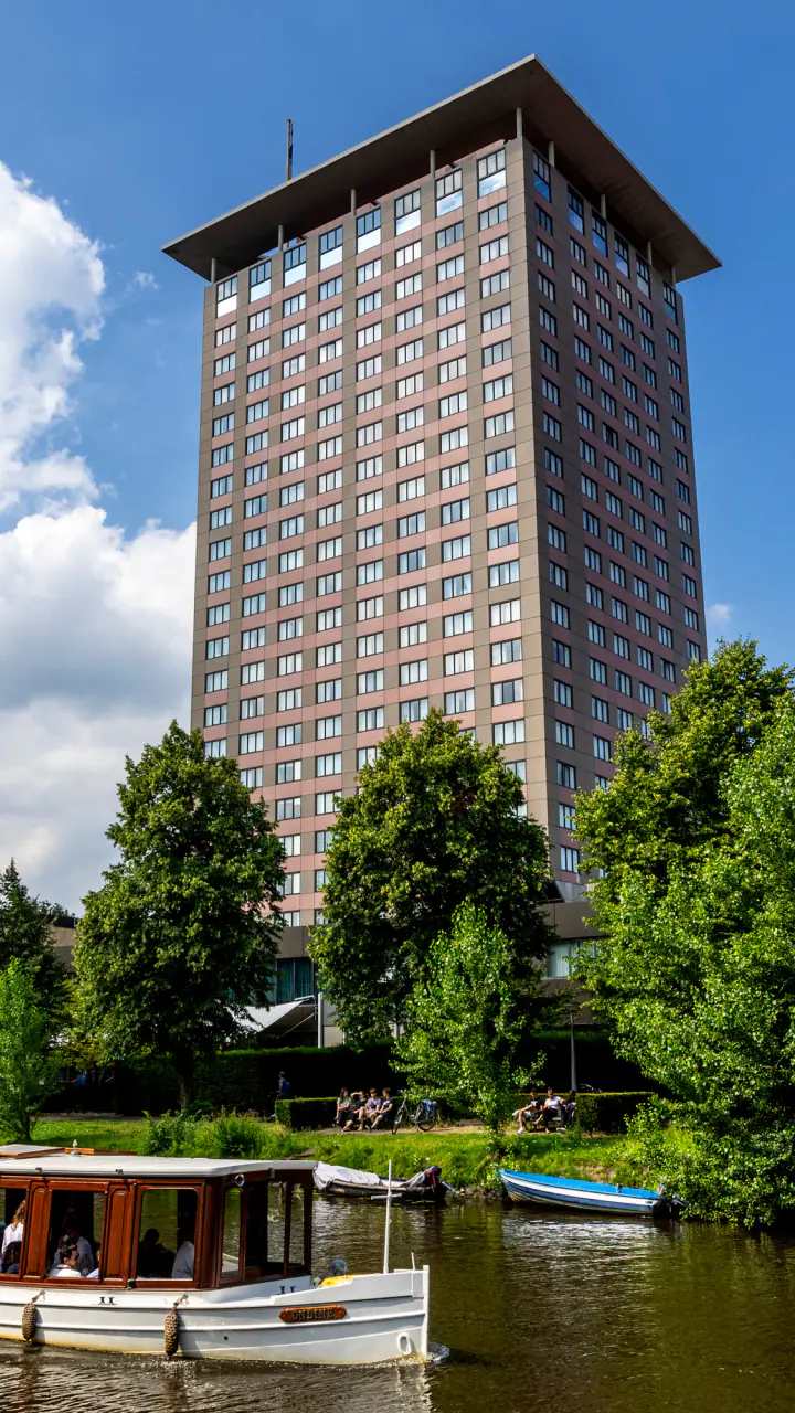 De toren van Hotel Okura boven de bomen langs het water, met een salonboot op de voorgrond