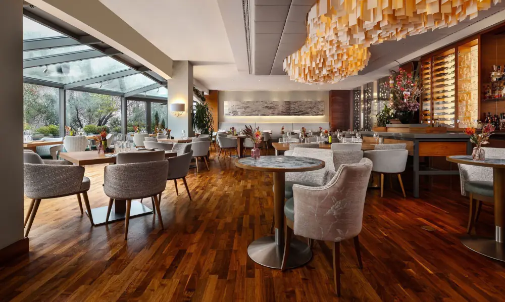 Serre Restaurant: een lichte zaal met houten vloer, ronde tafels en een glazen gevel