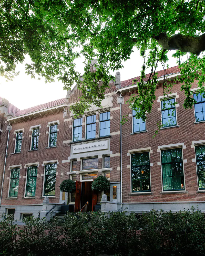 De bakstenen voorgevel achter de bomen, in het ochtendlicht
