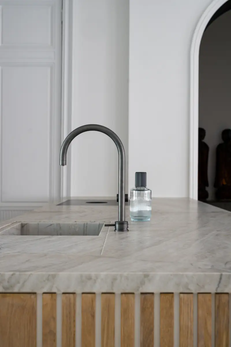 Curved tap in dark metal above an inset marble sink, with a glass carafe beside it