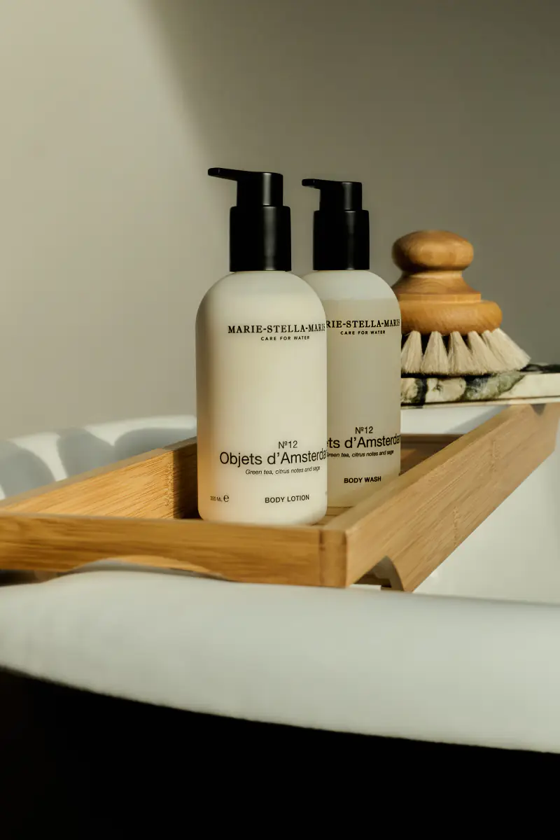 Bodylotion en douchegel in witte pompflessen op een houten badplank, met een borstel erachter