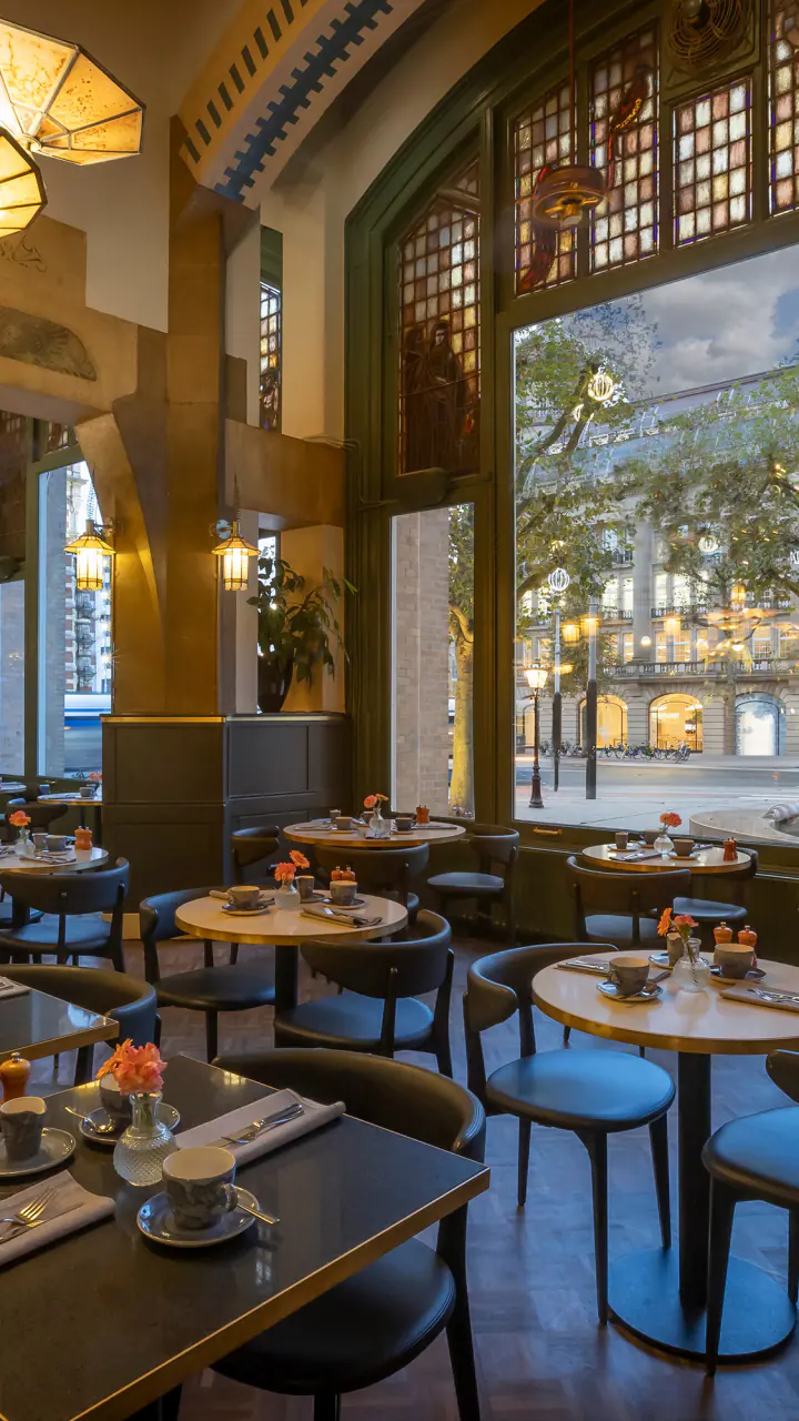 Café Americain met gedekte tafels, hoge glas-in-loodramen en grote hanglampen