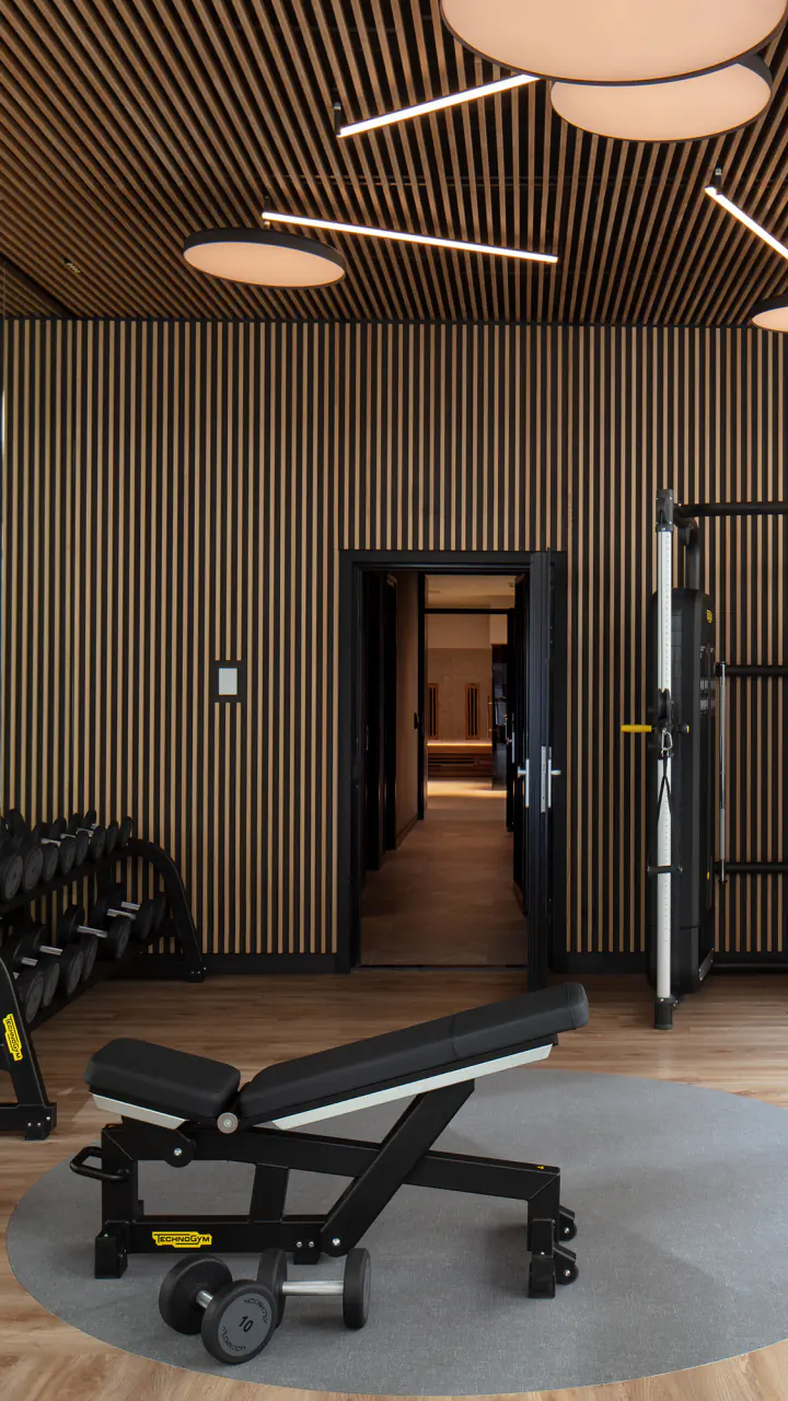 Fitnessruimte met losse gewichten, toestellen en een houten lattenwand