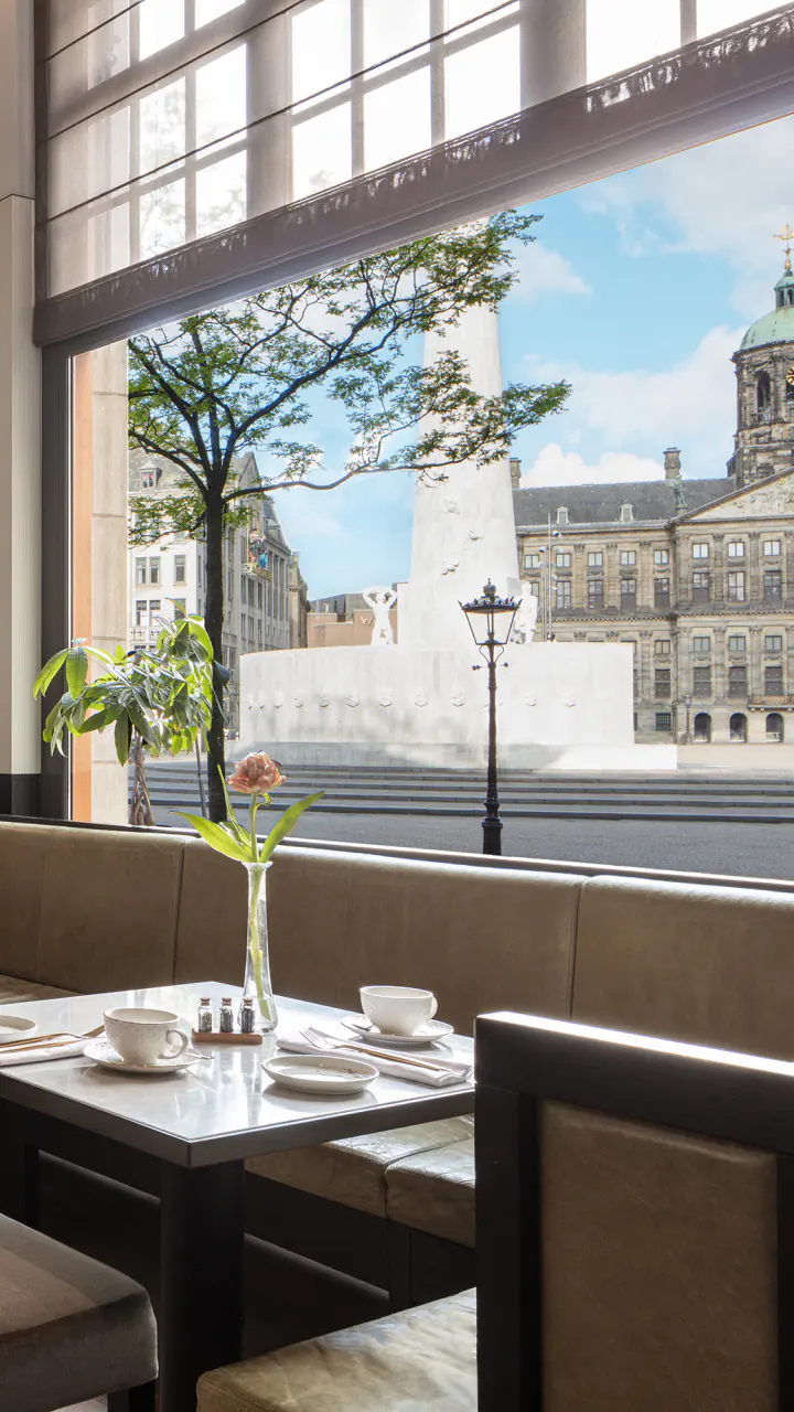 Grand café met grote ramen en uitzicht op de Dam en het Koninklijk Paleis