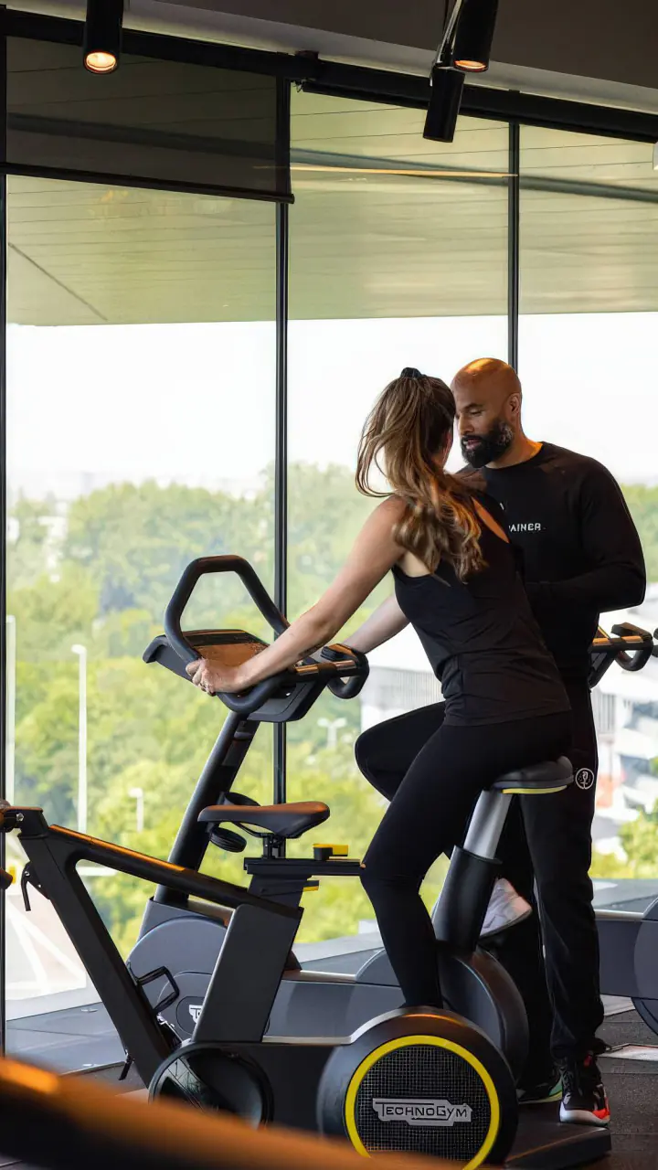 Een personal trainer helpt een gast op een hometrainer van Technogym in de gym van nhow, met uitzicht over de ringweg en het groen