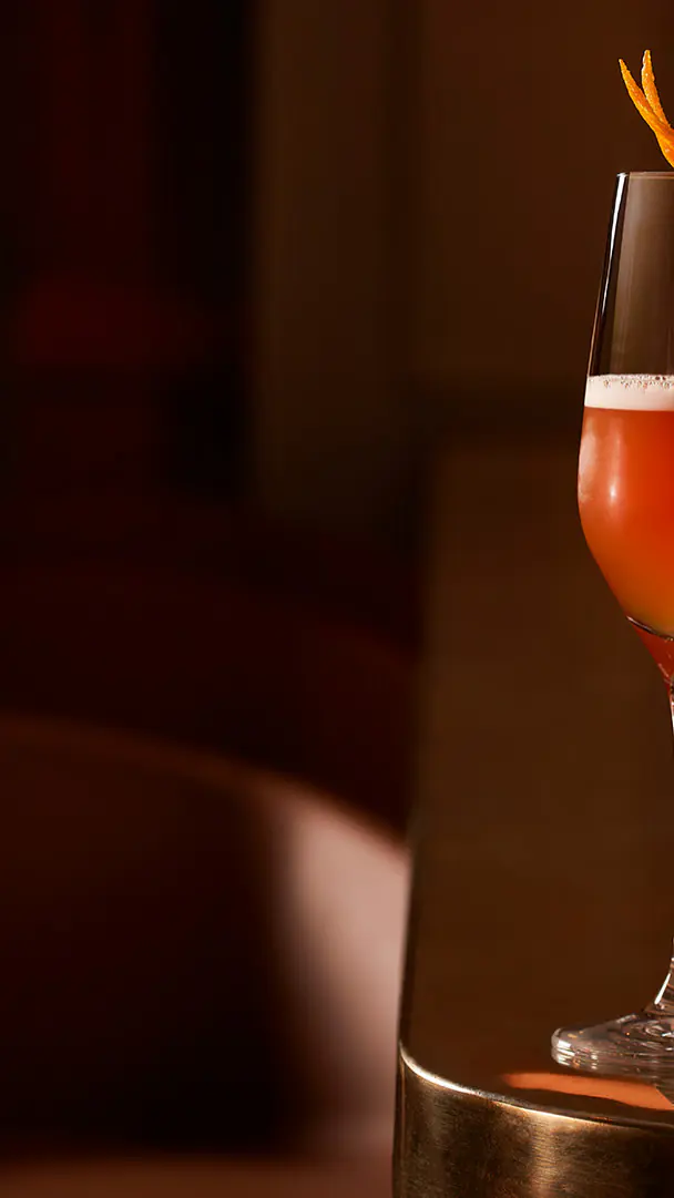 Een cocktail met een sinaasappelschil naast een schaaltje noten op de bar van Omber Bar