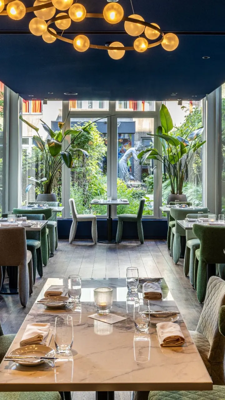 Restaurant Renvy met gedekte tafels, hoge ramen, planten en goudkleurige bollampen aan het plafond
