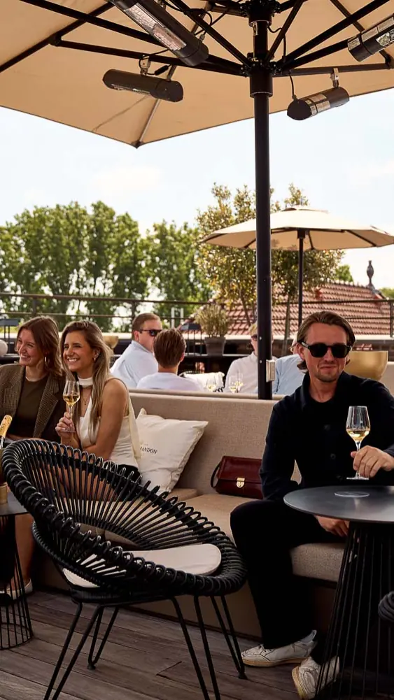 Gasten op het dakterras van Pillows onder parasols, met bomen op de achtergrond