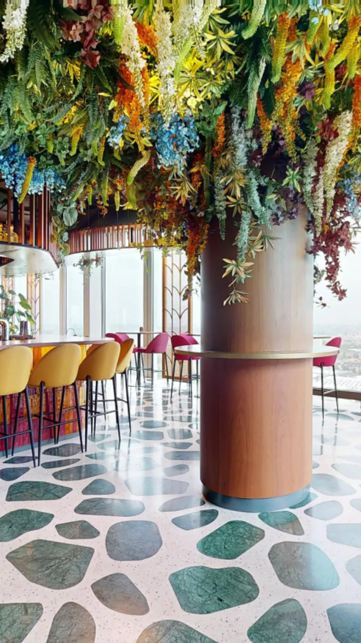De bar van Selva onder een dak van planten, met gele krukken en een vloer van groene en witte stenen