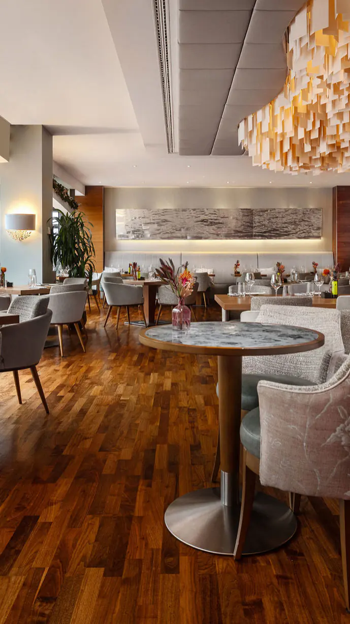 Serre Restaurant: een lichte zaal met houten vloer, ronde tafels en een glazen gevel