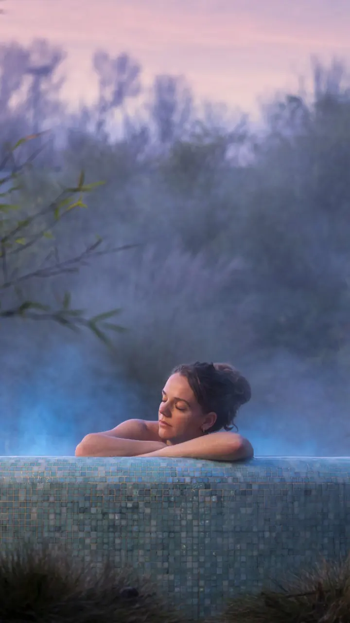 Een vrouw in een dampend buitenbad van Zuiver in de schemering, tussen het groen