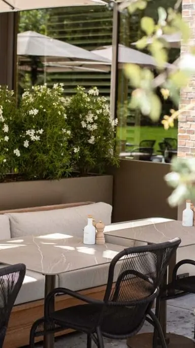 Het terras van Spring Café Brasserie met witte banken, tafels en veel groen