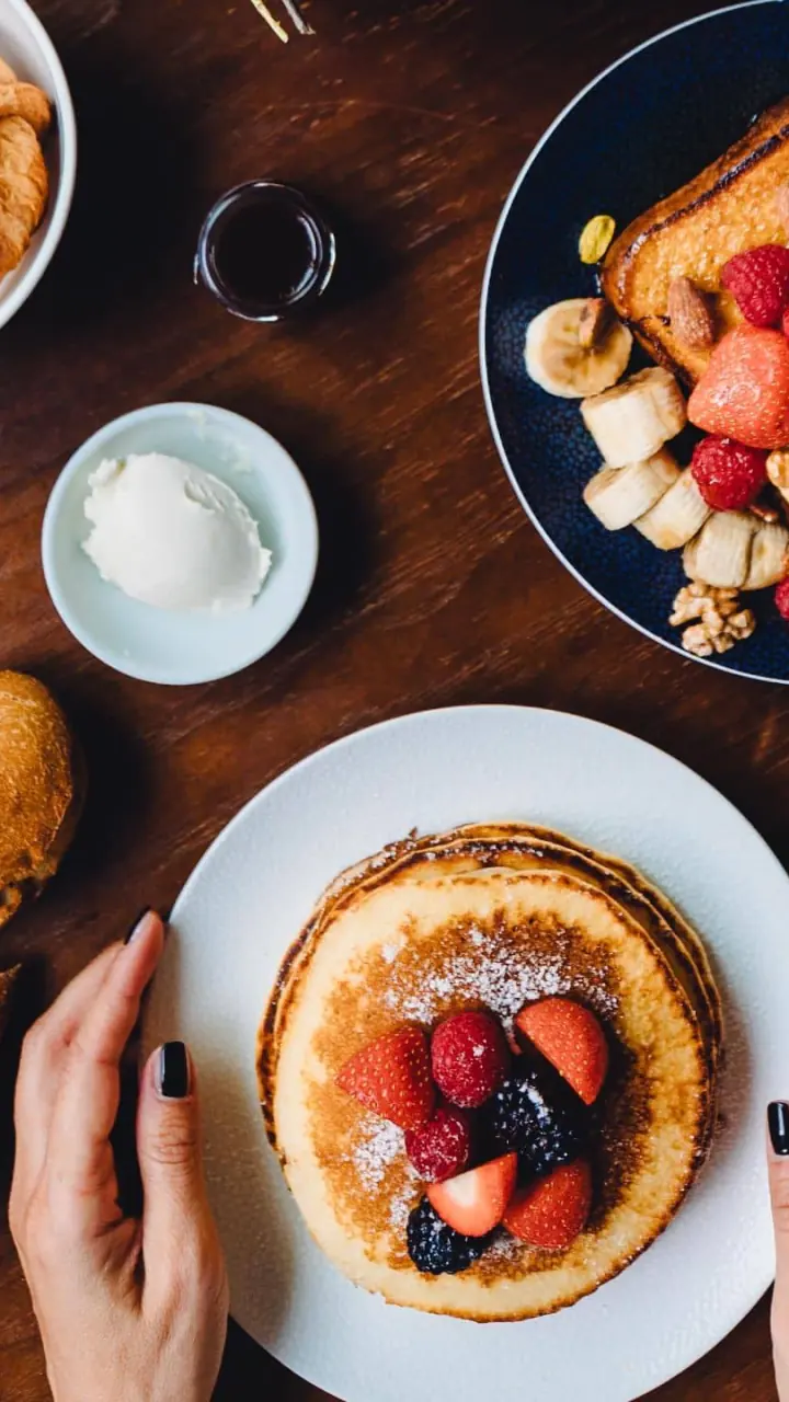 Ontbijt van bovenaf: croissants, pannenkoeken, fruit en koffie op een houten dienblad