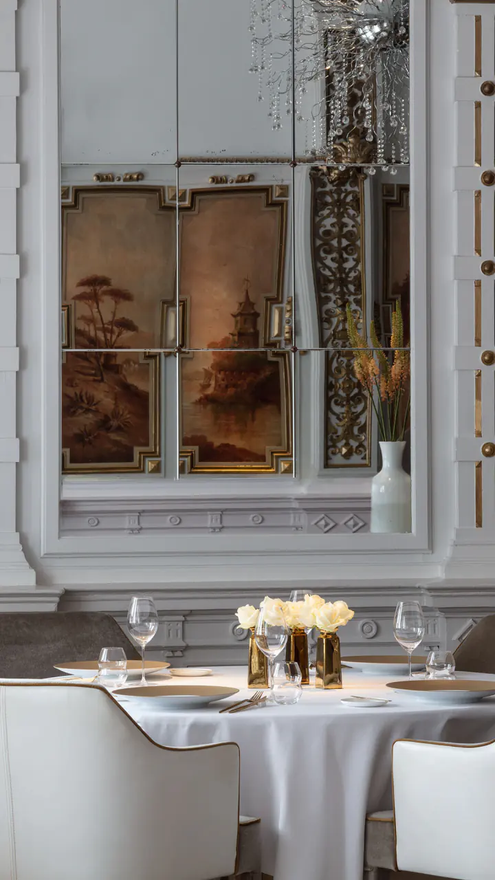 De Witte Zaal van The White Room, fine dining in Amsterdam centrum: gedekte ronde tafels voor beschilderde wandpanelen met goudlijsten