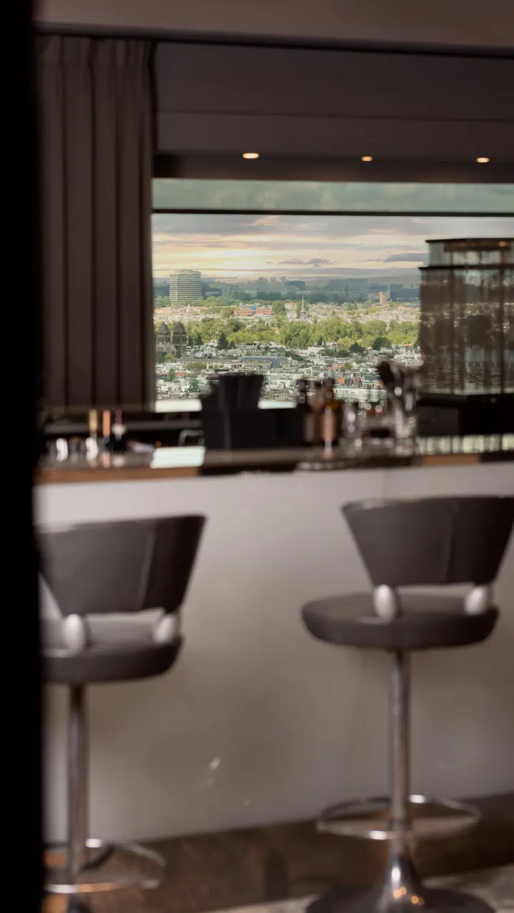 Twenty Third Bar met barkrukken aan een witte bar en een raam met uitzicht over Amsterdam